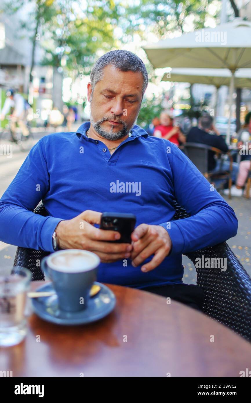 man uses smart phone while having drinks coffee in cafe outside Stock Photo