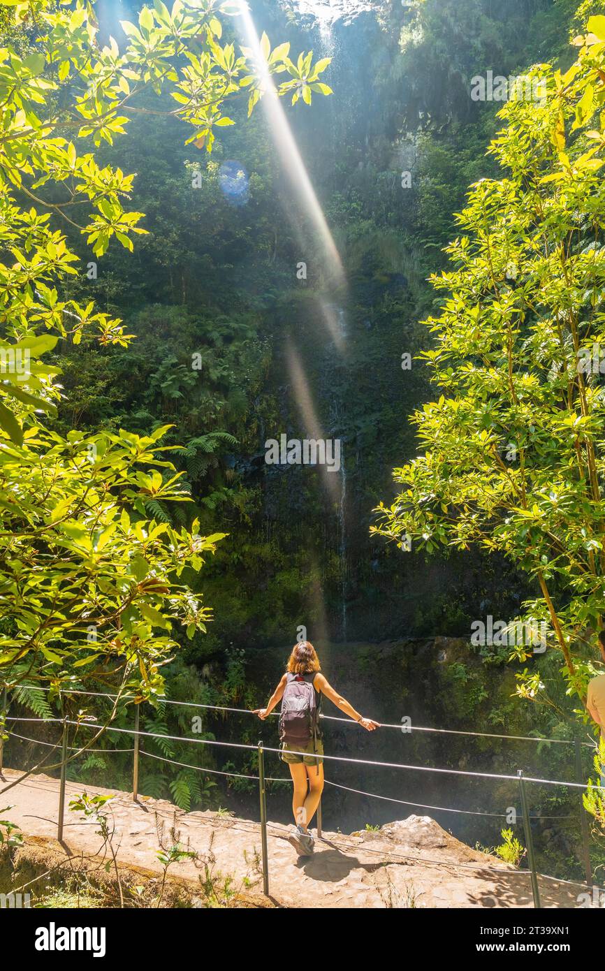 Eine junge Frau betrachtet im Sommer einen kleinen Wasserfall an der Levada do Caldeirao Verde, Queimadas, Madeira Stock Photo