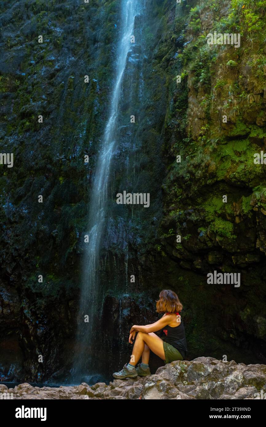 Unbekannte junge Frau sitzt im Wasserfall an der Levada do Caldeirao Verde, Queimadas, Madeira Stock Photo