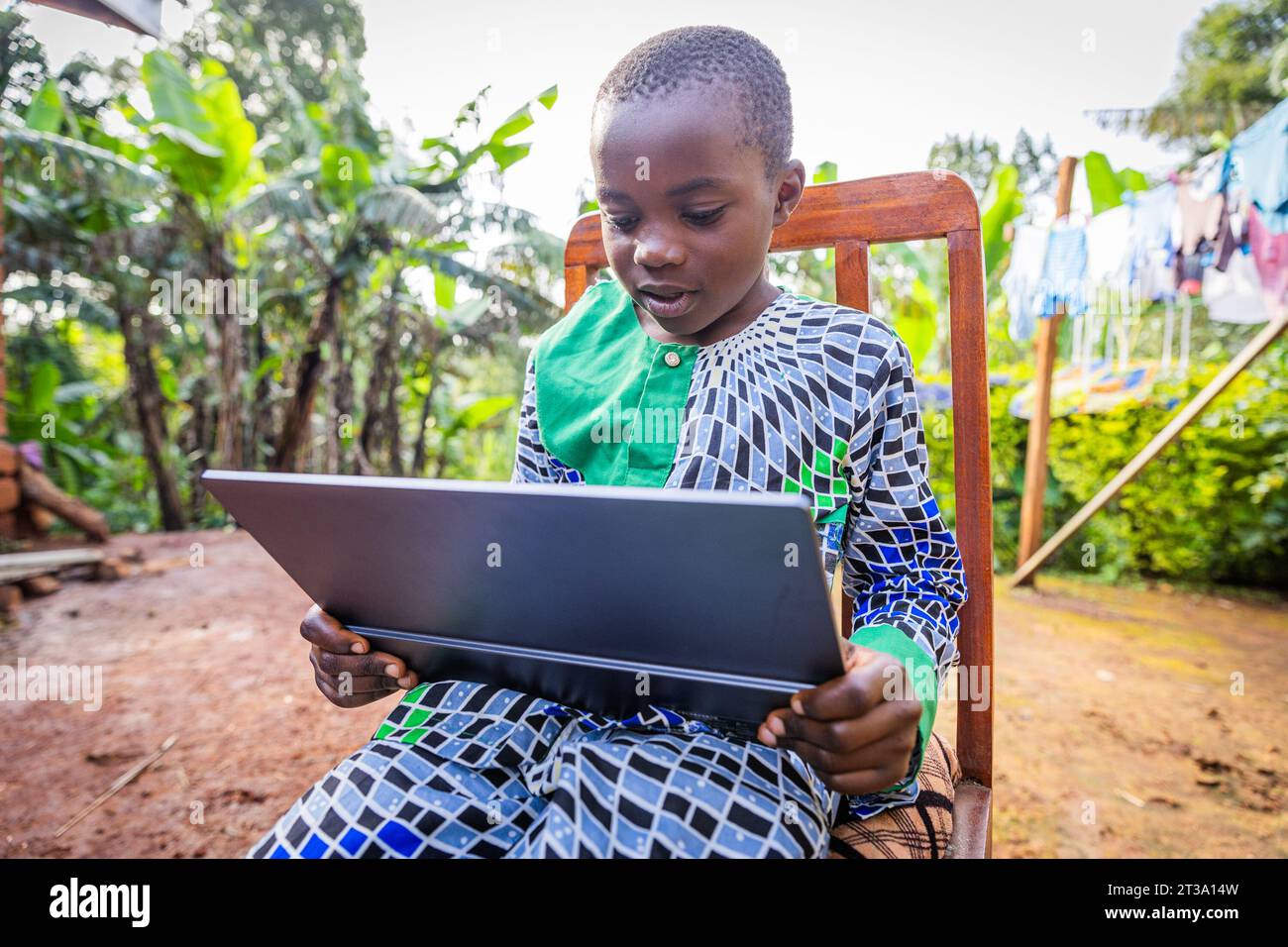 African young student sitting outdoors, keen on his tablet rehearsing his lessons. Stock Photo