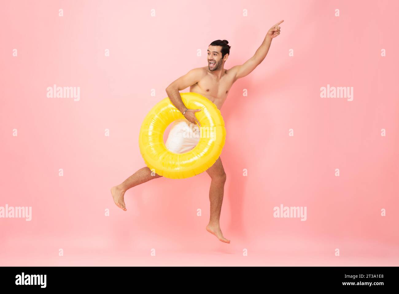 Summer portrait of happy handsome shirtless Caucasian man jumping with hand pointing up studio shot isolated on pink color background Stock Photo