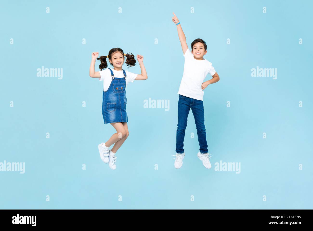 Mixed race Asian boy and girl playing by jumping in the air against light blue color isolated background studio shot Stock Photo