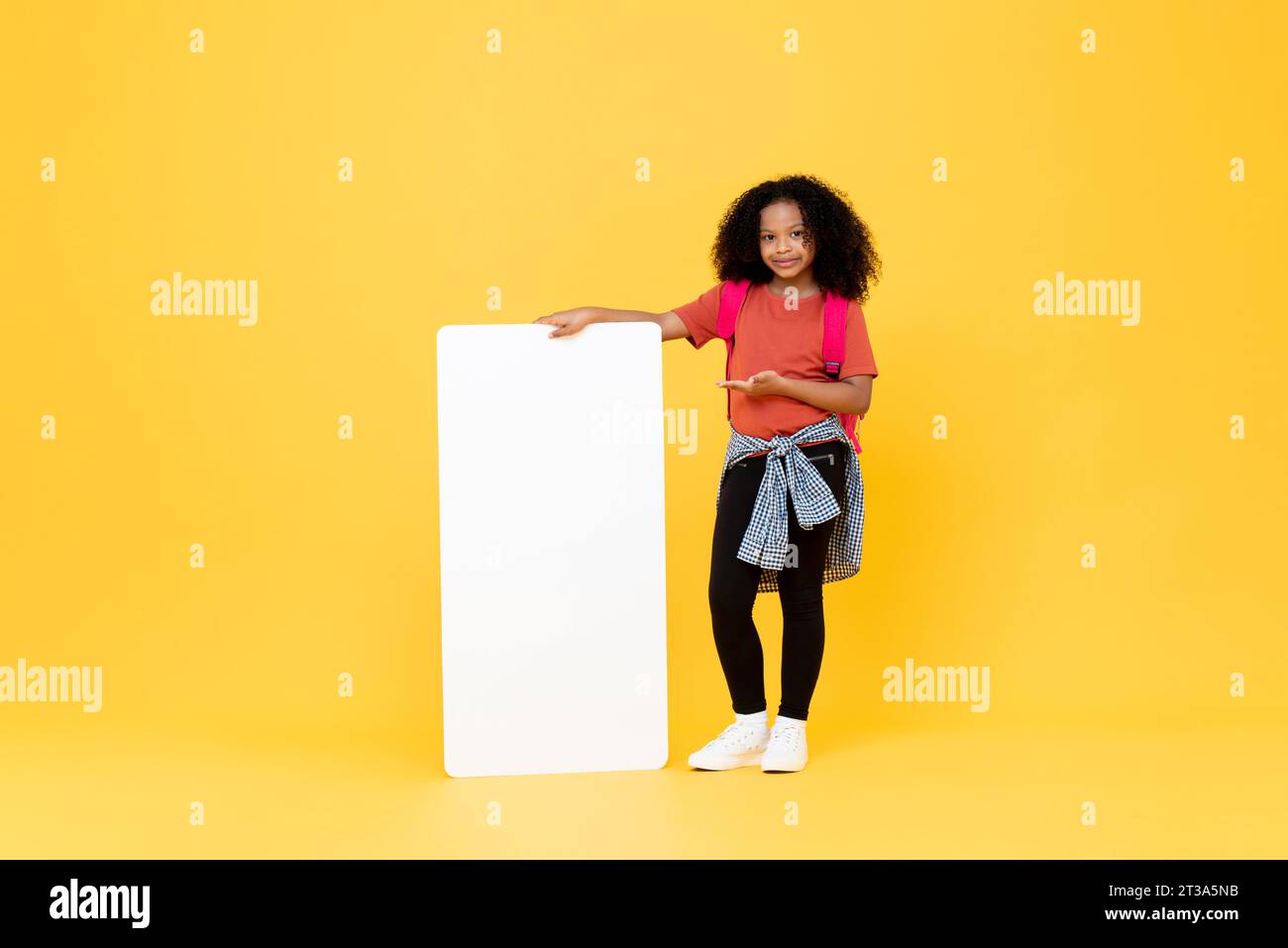 Cute African American female kid standing and pointing hand to empty board with space for text in yellow color isolated background studio shot Stock Photo
