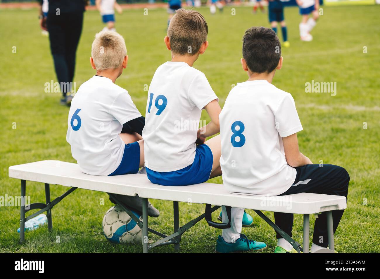 Substitute soccer players in kids' soccer teams. Boys watching football league match from soccer bench. School sports teams on children soccer league Stock Photo