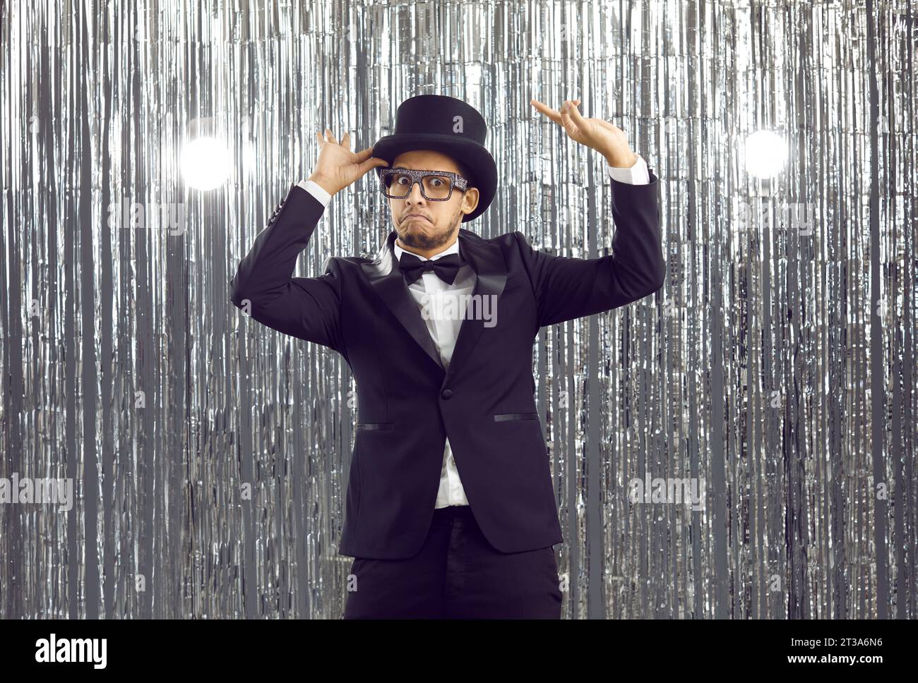 Goofy man in a tuxedo, bow tie, glasses and top hat dancing at a party with a funny face expression Stock Photo