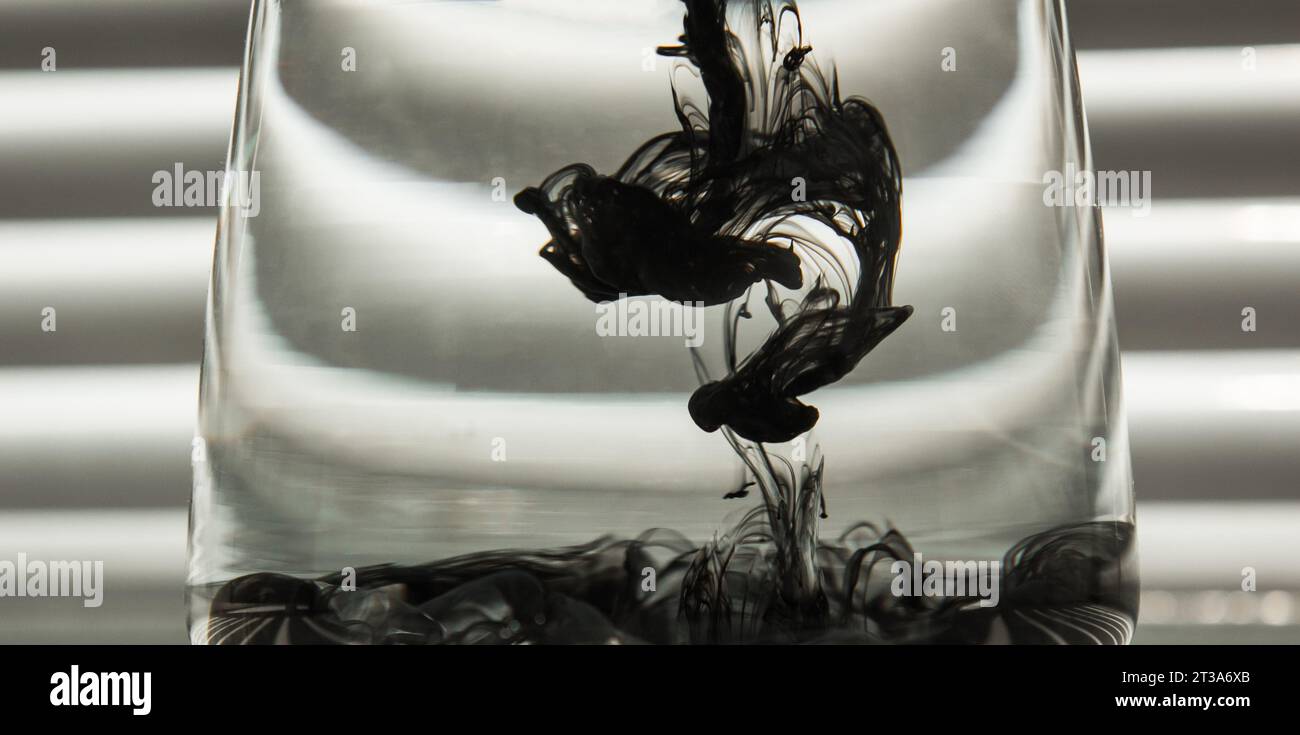 Light Rays Ink a cloud of ink in a transparent glass cup with clear water against the ...