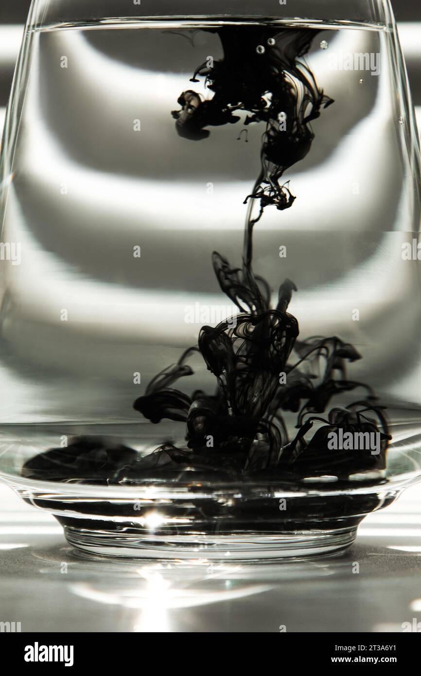Light Rays Ink a cloud of ink in a transparent glass cup with clear water against the ...