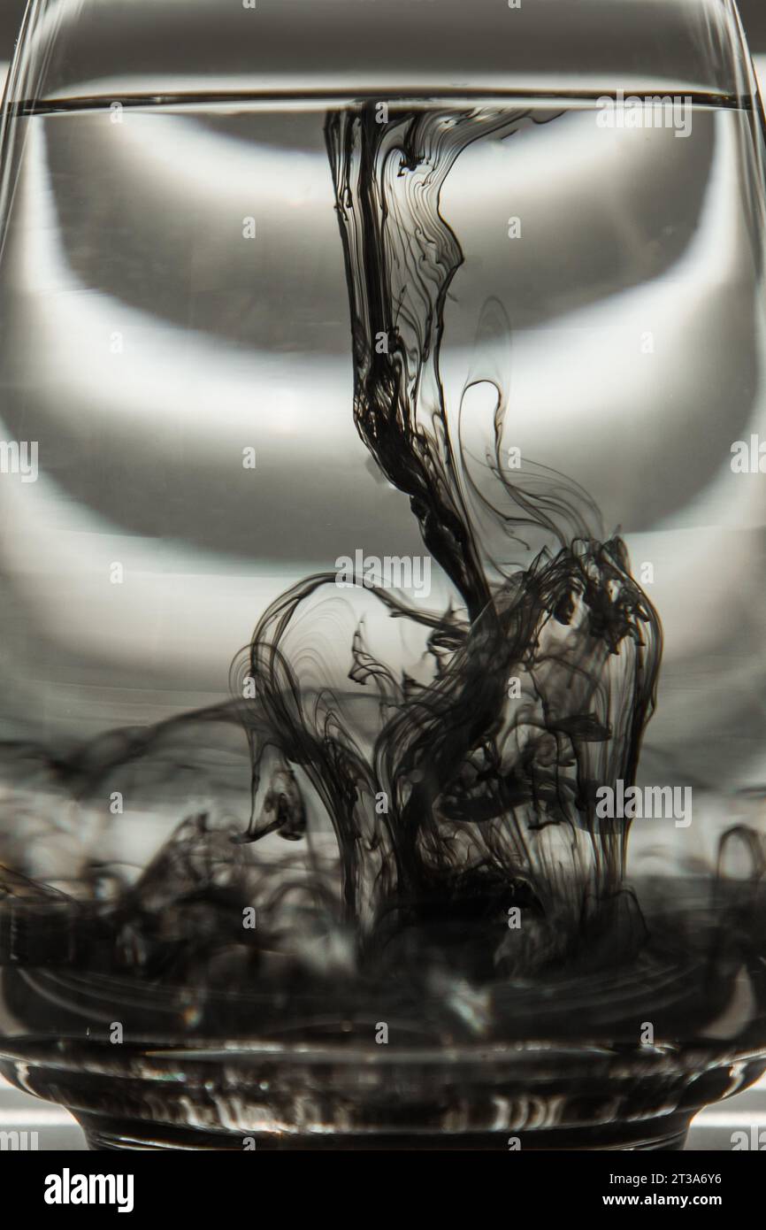 Light Rays Ink a cloud of ink in a transparent glass cup with clear water against the ...