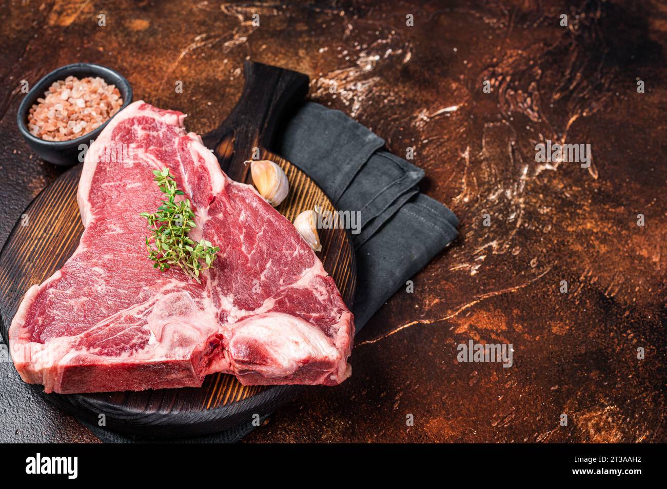 Raw Porterhouse steak, marbled beef meat on a wooden board. Dark background. Top view. Copy space. Stock Photo