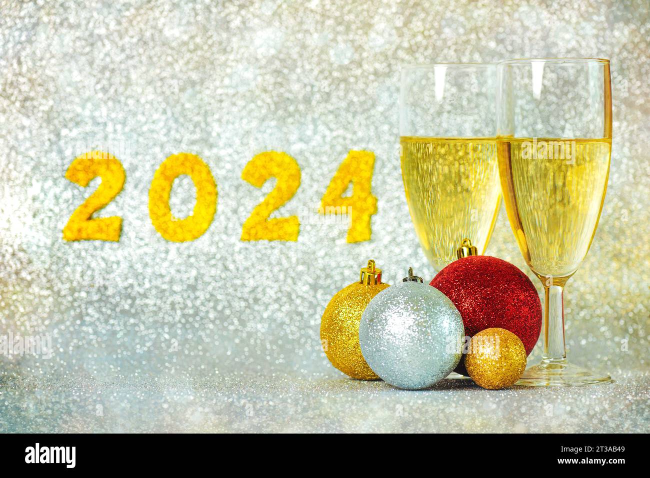 Happy new year 2024. Two glasses of champagne with christmas balls and golden numbers with the number 2024 on a silver background bokeh. New Years Eve Stock Photo