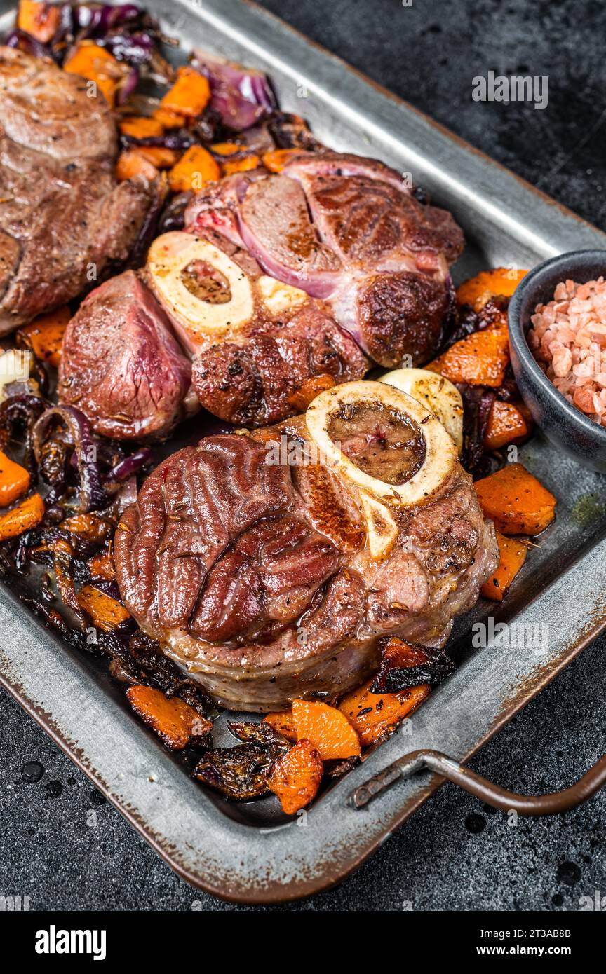 Italian braised veal shank steak Ossocbuco with vegetable sauce on steel tray. Black background. Top view. Stock Photo