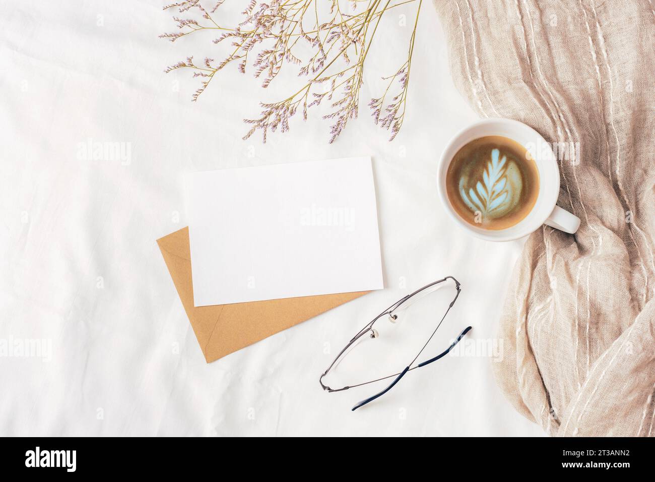 Coffee cup, envelope with blank card, glasses and small flowers on white linen. Cozy workplace, breakfast, comfort, hygge concept. Top view, flat lay, Stock Photo