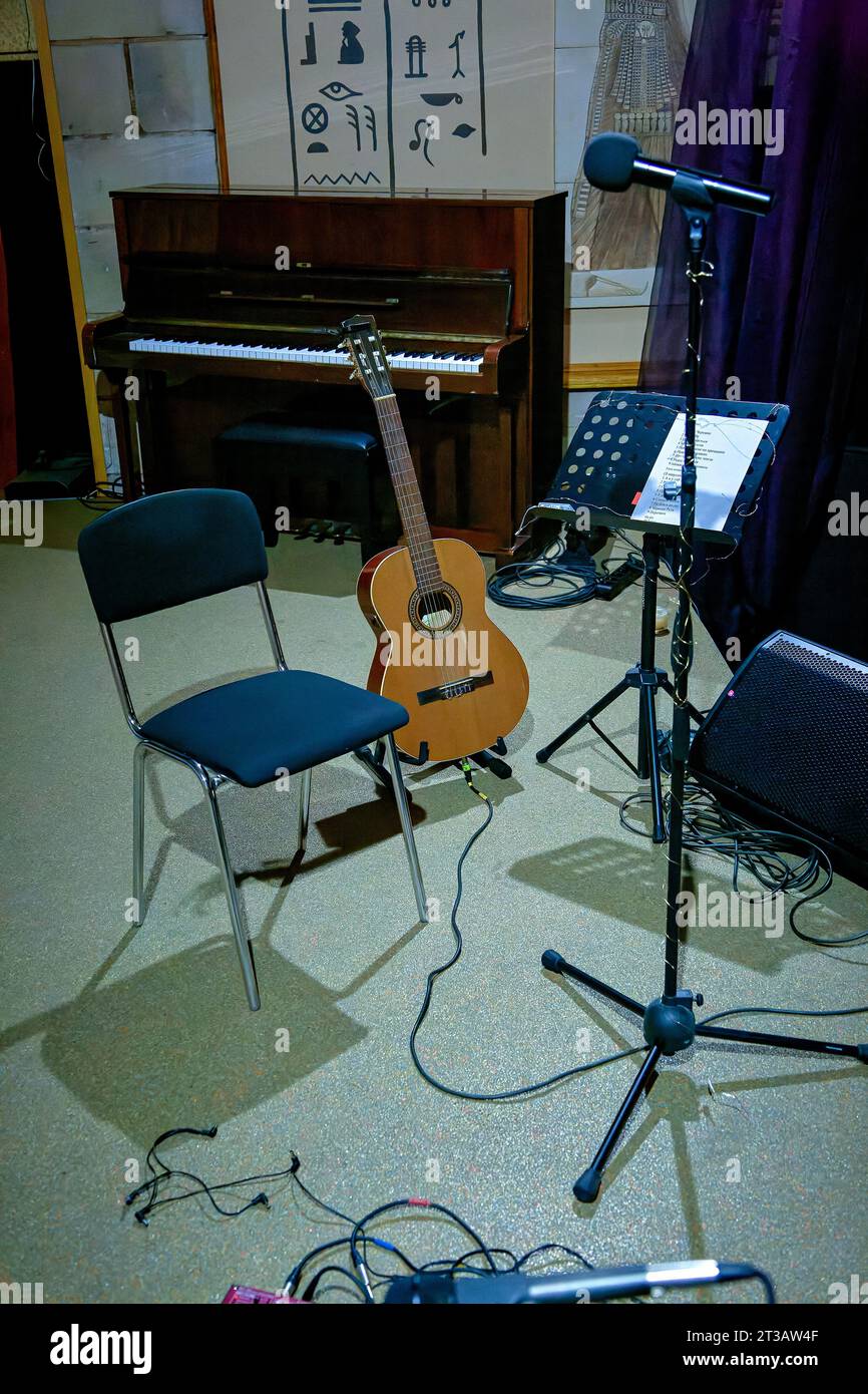 An image of an acoustic guitar stands on stage near a music stand Stock Photo
