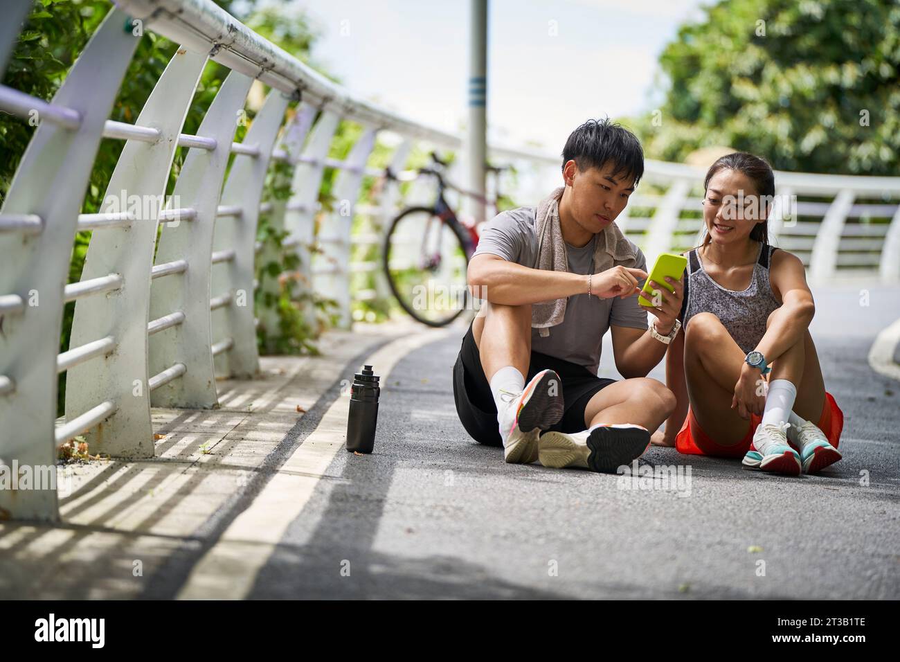 young asian couple sharing cellphone photos while taking a break during outdoor exercise Stock Photo