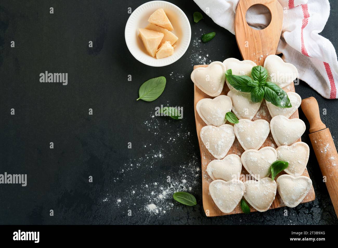 Italian ravioli pasta in heart shape. Tasty raw ravioli with flour and basil on dark background. Food cooking ingredients background. Valentines or Mo Stock Photo