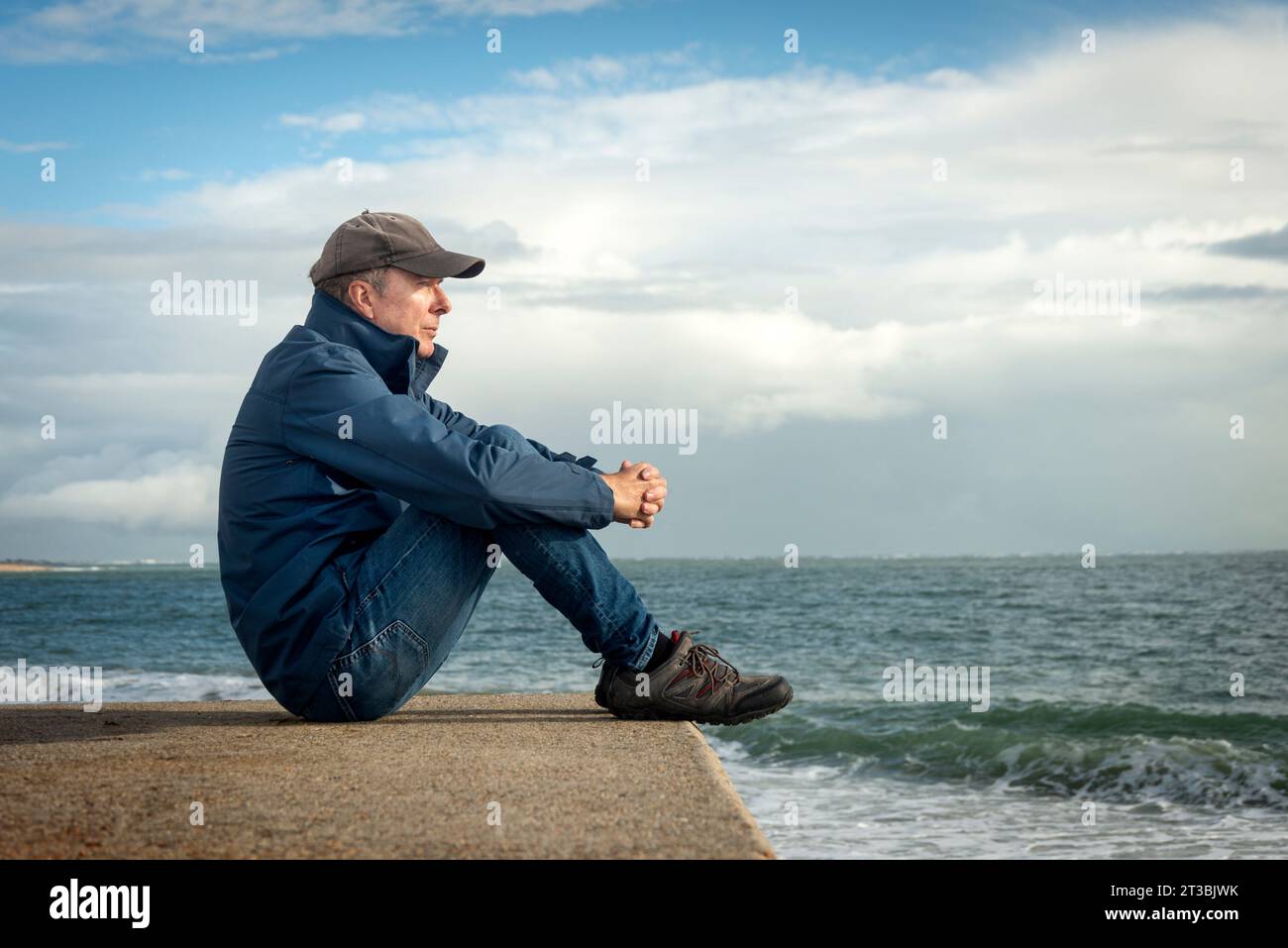 man sitting looking out over the ocean. Enjoying peace in nature. Contemplation. Stock Photo