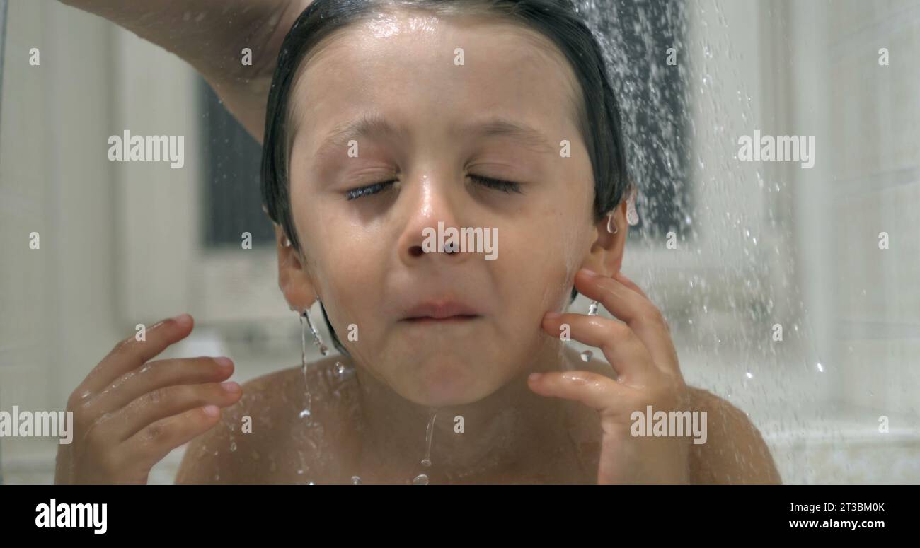 Displeased small boy underneath water shower head while grimacing in