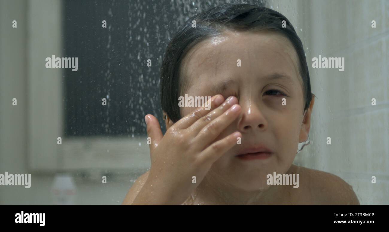 Child touching eye with finger while underneath of shower head with