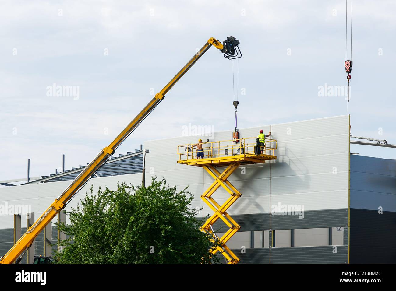 Sandwich panels wall assembly using telescopic boom crane and yellow self propelled scissor lift platform Stock Photo