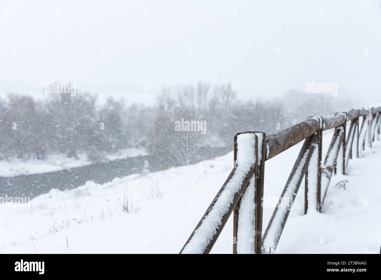Wooden fence covered by snow beside a river under a heavy snowfall in winter Stock Photo