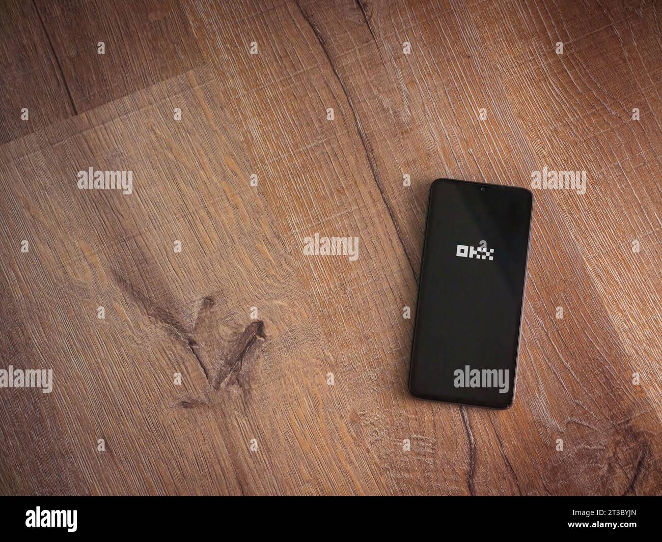 Lod, Israel - July 16,2023: OKX app launch screen on smartphone on wooden background. Top view flat lay with copy space. Stock Photo