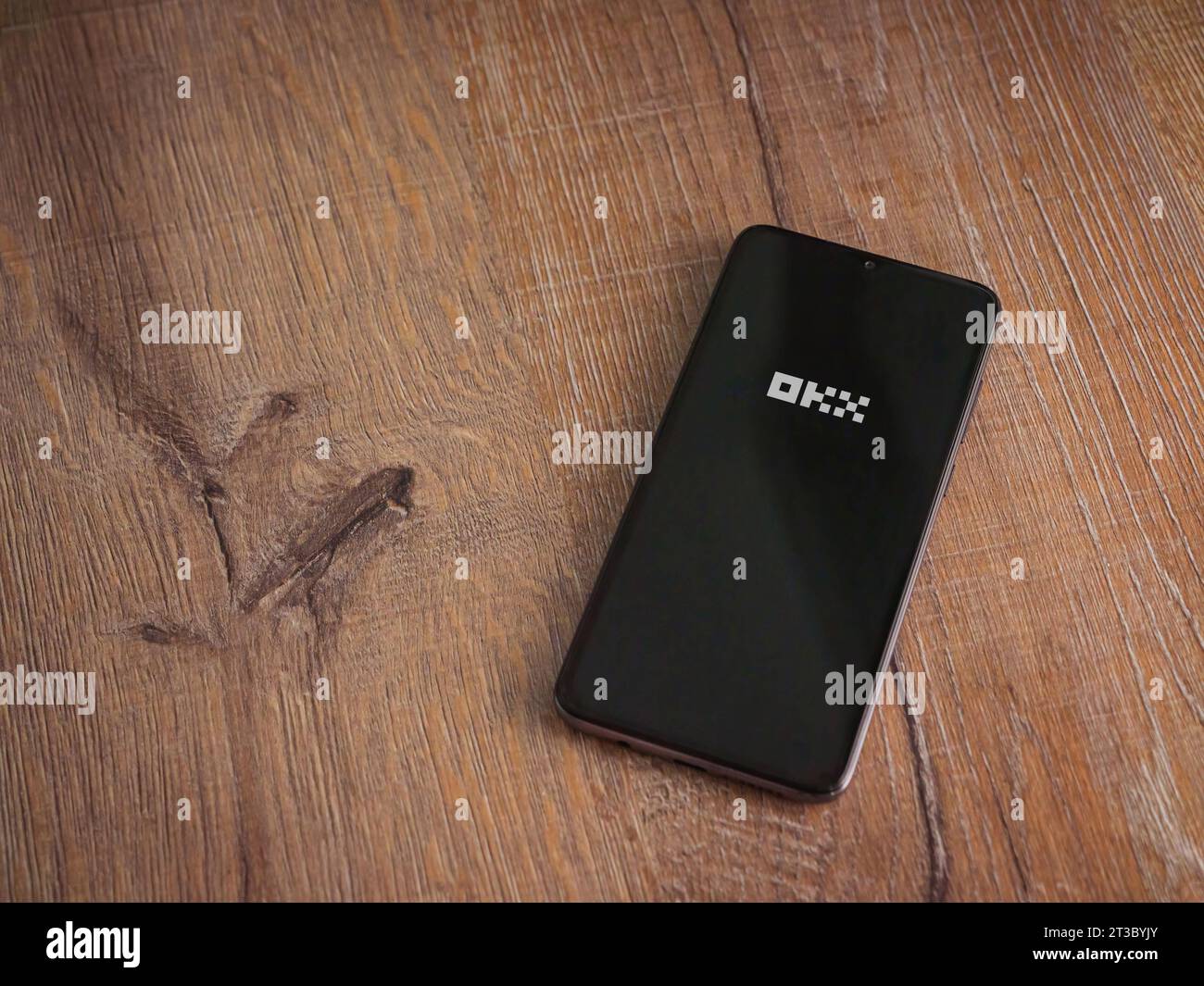 Lod, Israel - July 16,2023: OKX app launch screen on smartphone on wooden background. Top view flat lay with copy space. Stock Photo