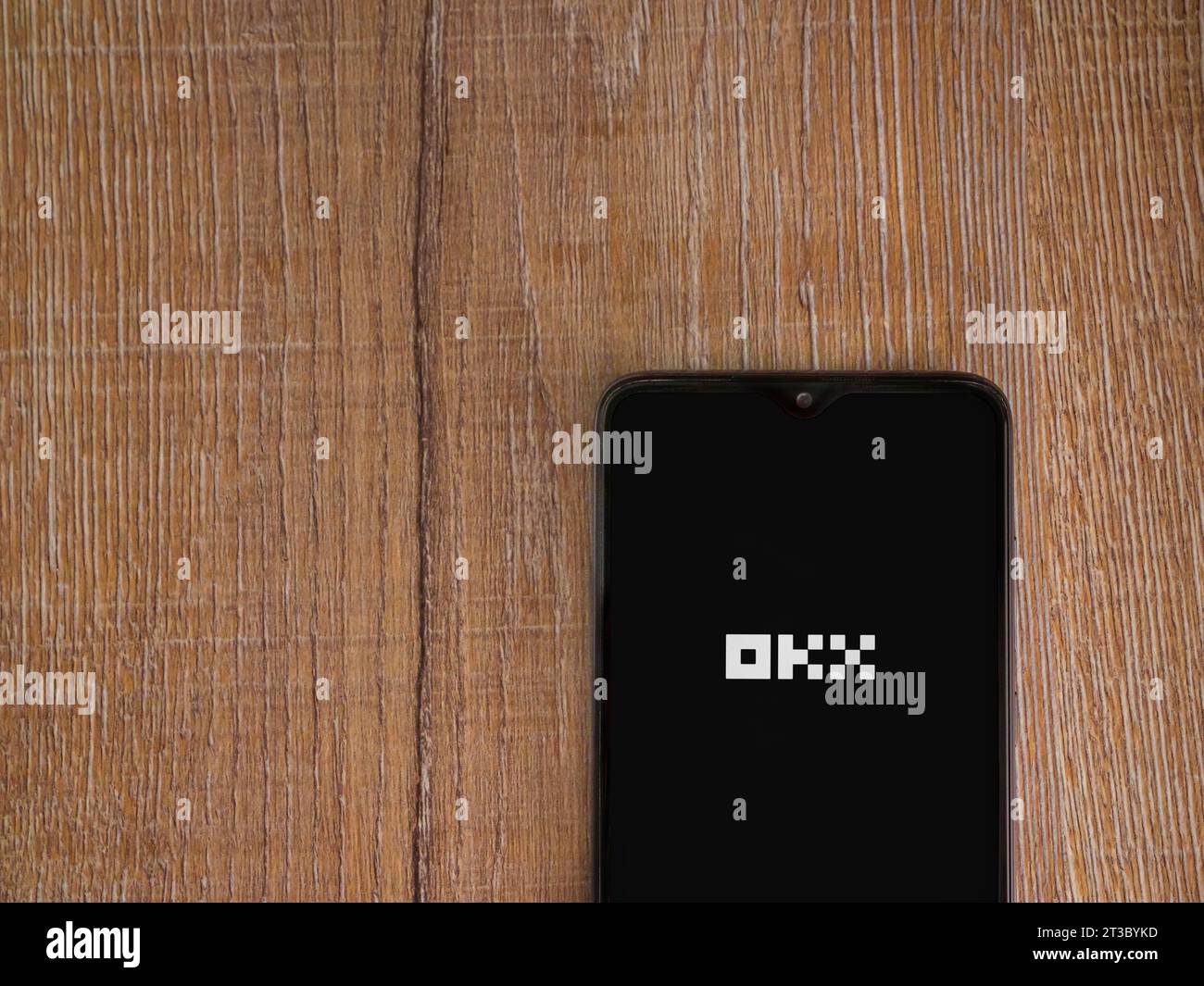 Lod, Israel - July 16,2023: OKX app launch screen on smartphone on wooden background. Top view flat lay with copy space. Stock Photo