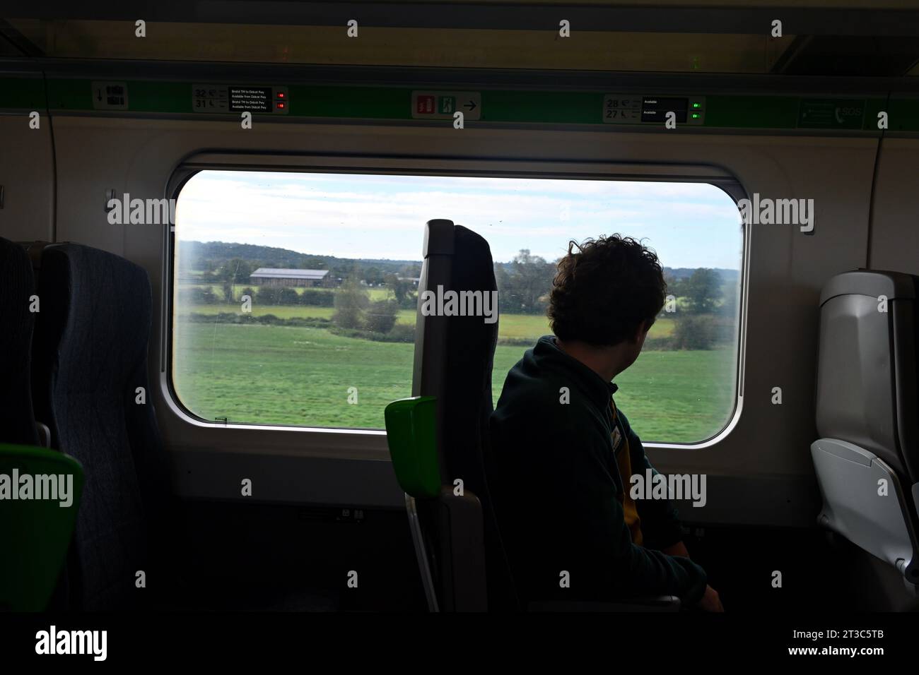 Silhouette of train passenger looking out of window with green fields of Wiltshire countryside, UK Stock Photo