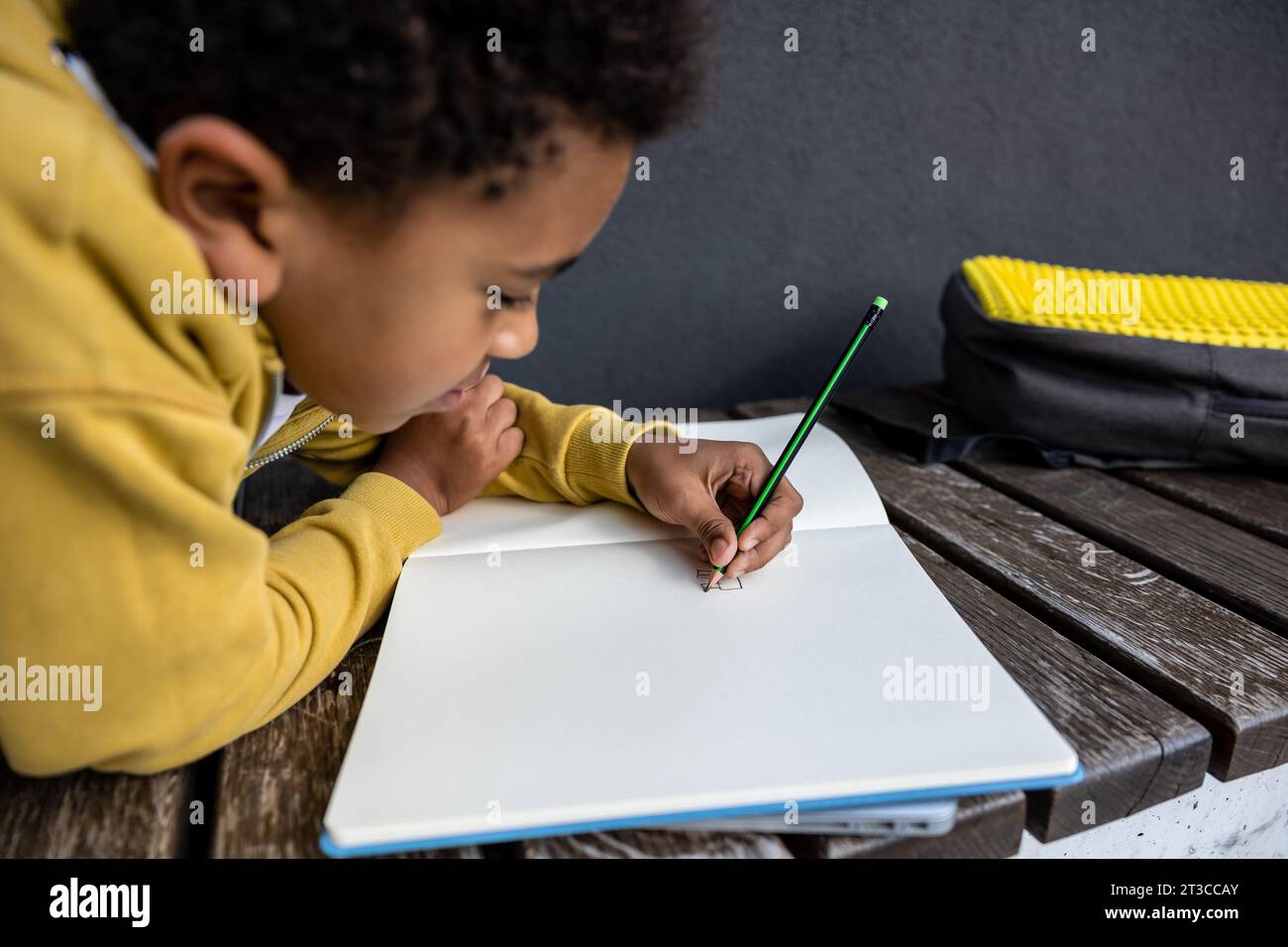 Schoolboy in yellow hoodie looking involved while doing homework Stock ...