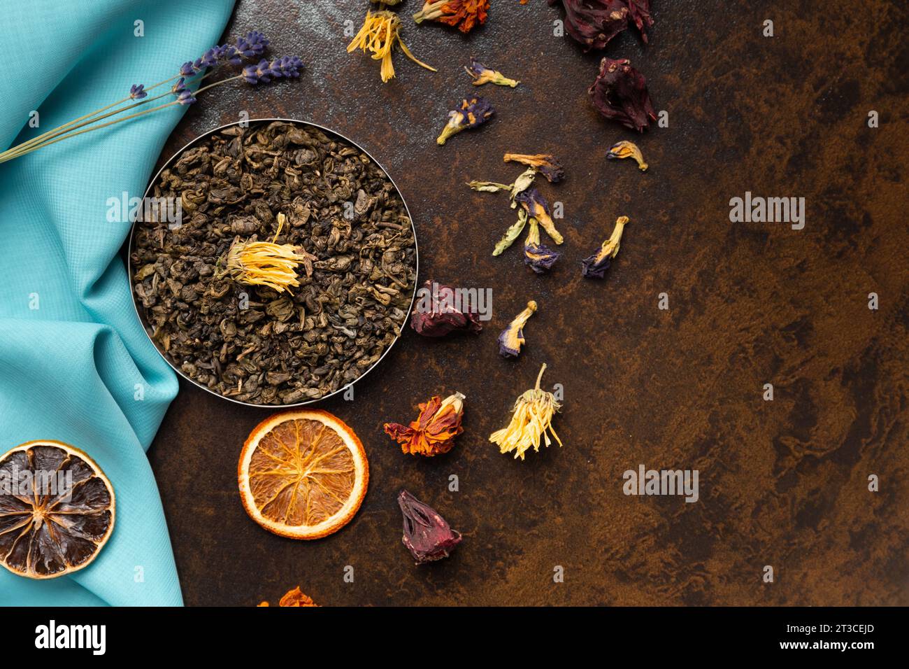 Composition of green, flower tea and dried orange slices on blue and brown backgrounds top view. Large-leaf tea, dried flowers and citrus chips Stock Photo