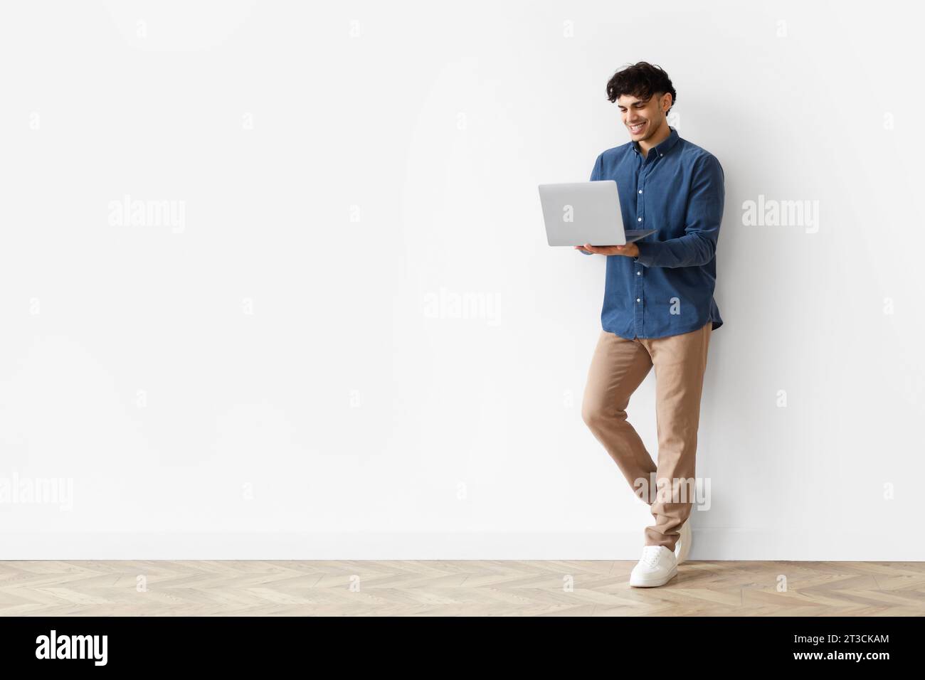 Young Arab Guy Using Laptop Leaning On White Studio Wall Stock Photo