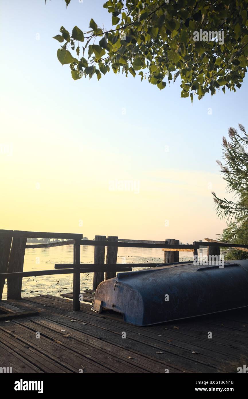 Boat  on a wooden pier by the lakeshore next to reeds at sunset Stock Photo