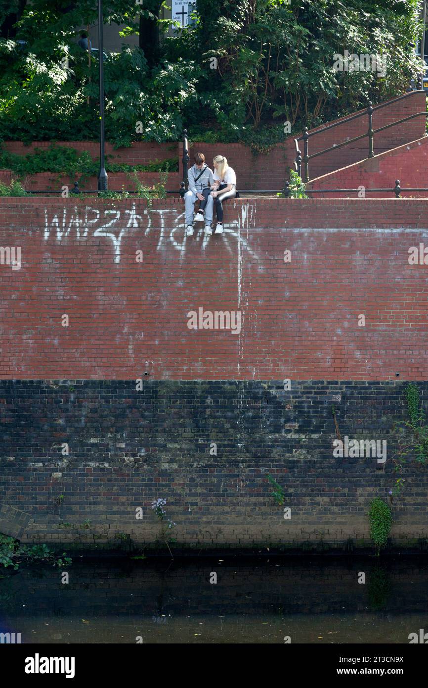 Young couple sitting on high wall above River Irwell, Manchester Stock Photo