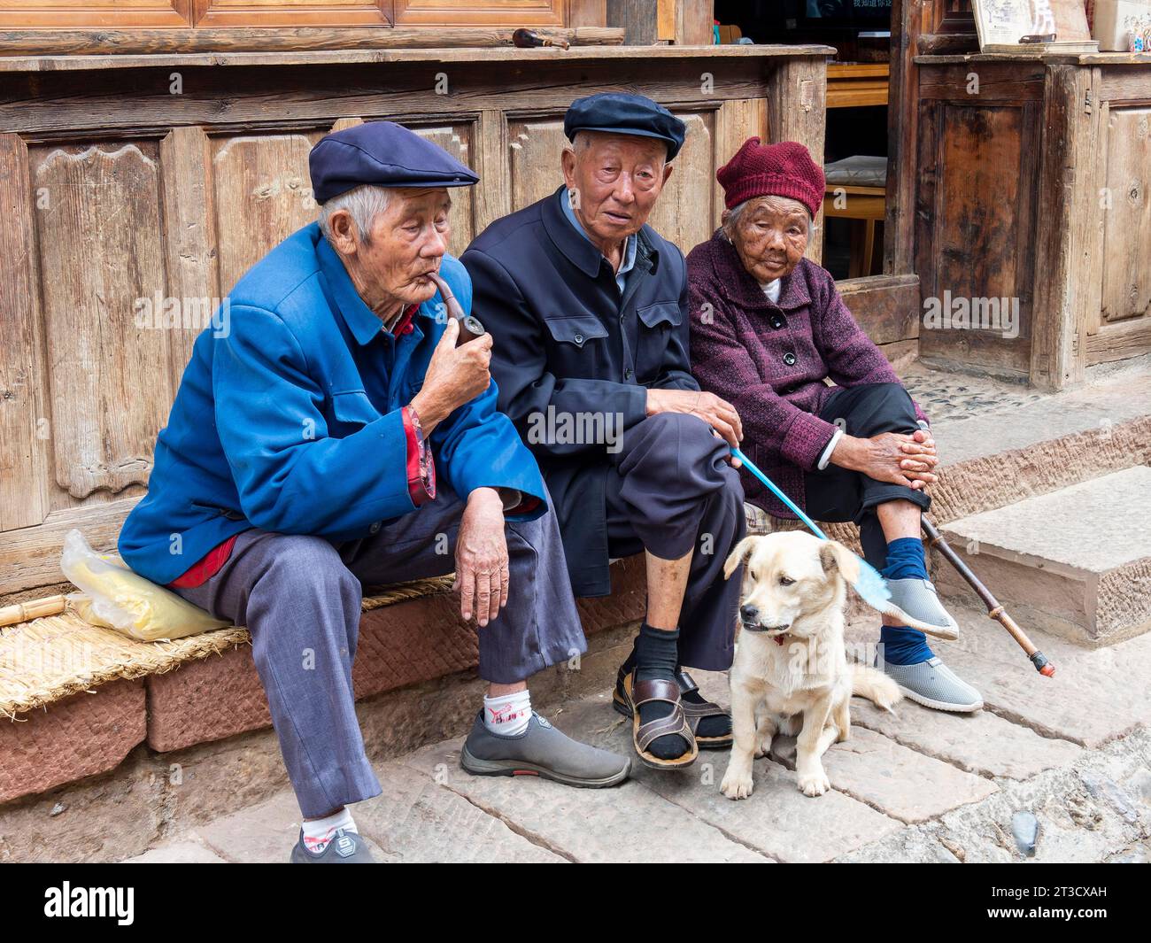 Old people sitting in front of the house, Chinese pensioners with dog, Shaxi, Yunnan, China Stock Photo