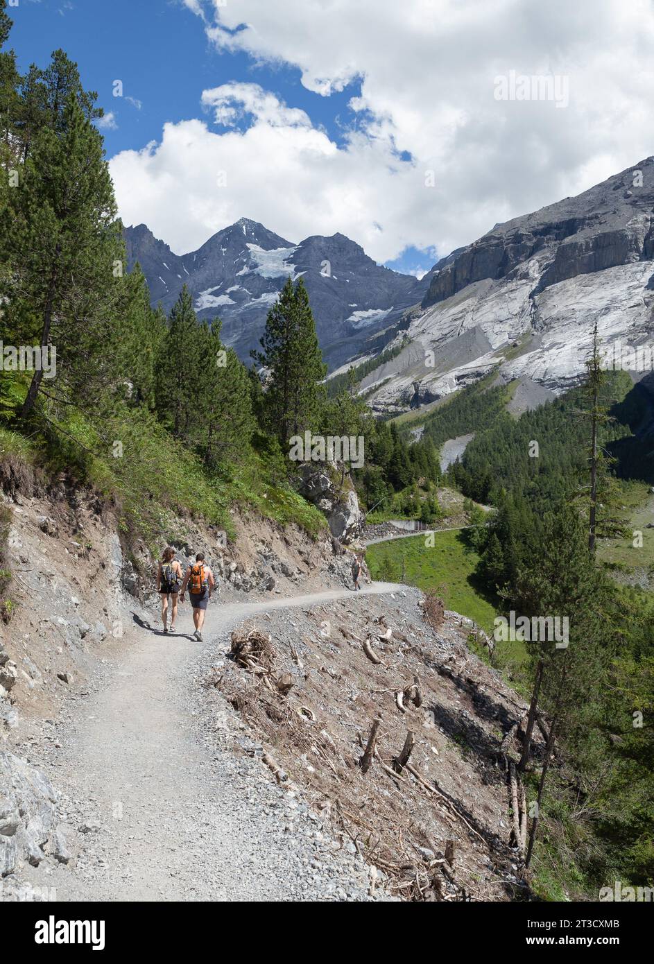 Kandersteg, Switzerland–Aug 3,2023: White people hiking on a curved path with snow mountain Stock Photo