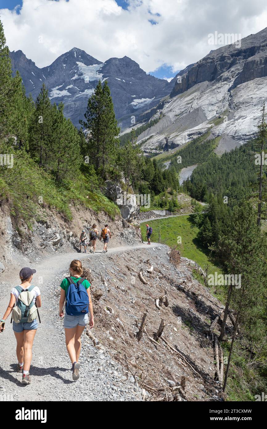 Kandersteg, Switzerland–Aug 3,2023: White people hiking on a curved path with snow mountain Stock Photo