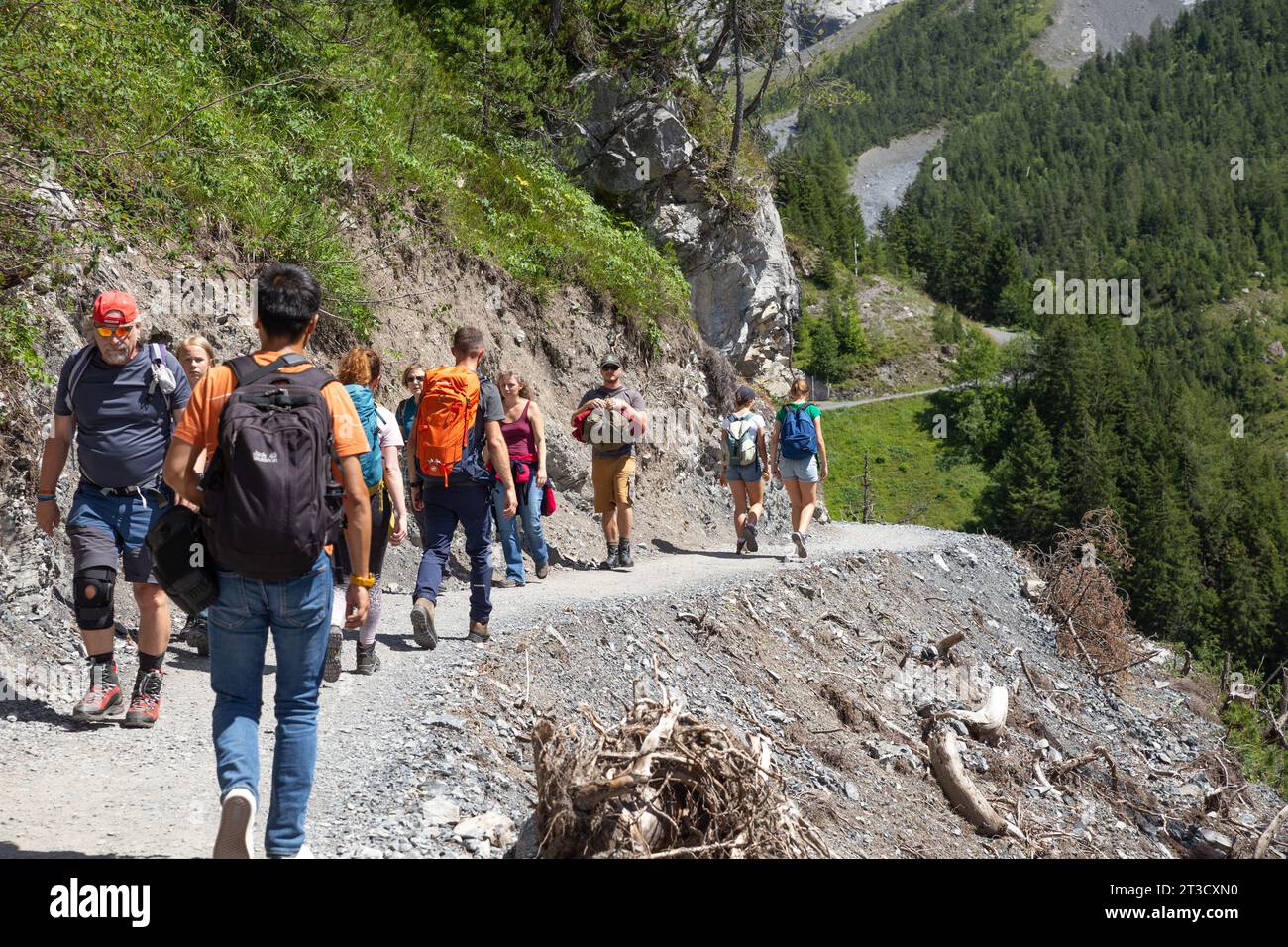 Kandersteg, Switzerland–Aug 3,2023: group of people hiking on a curved edging path with snow mountain Stock Photo