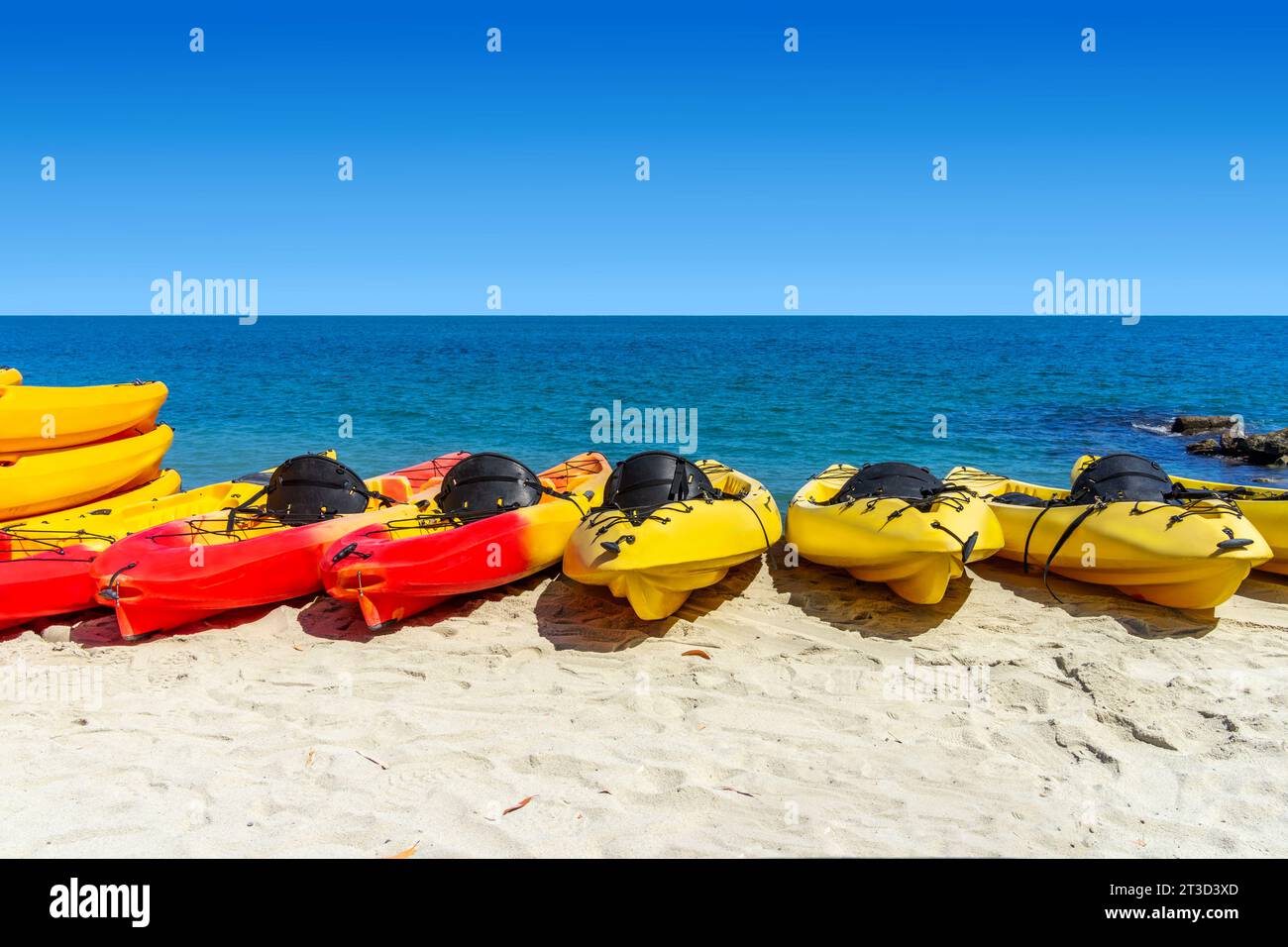 Red and yellow kayaks on the beach with the ocean and sky in the background Stock Photo