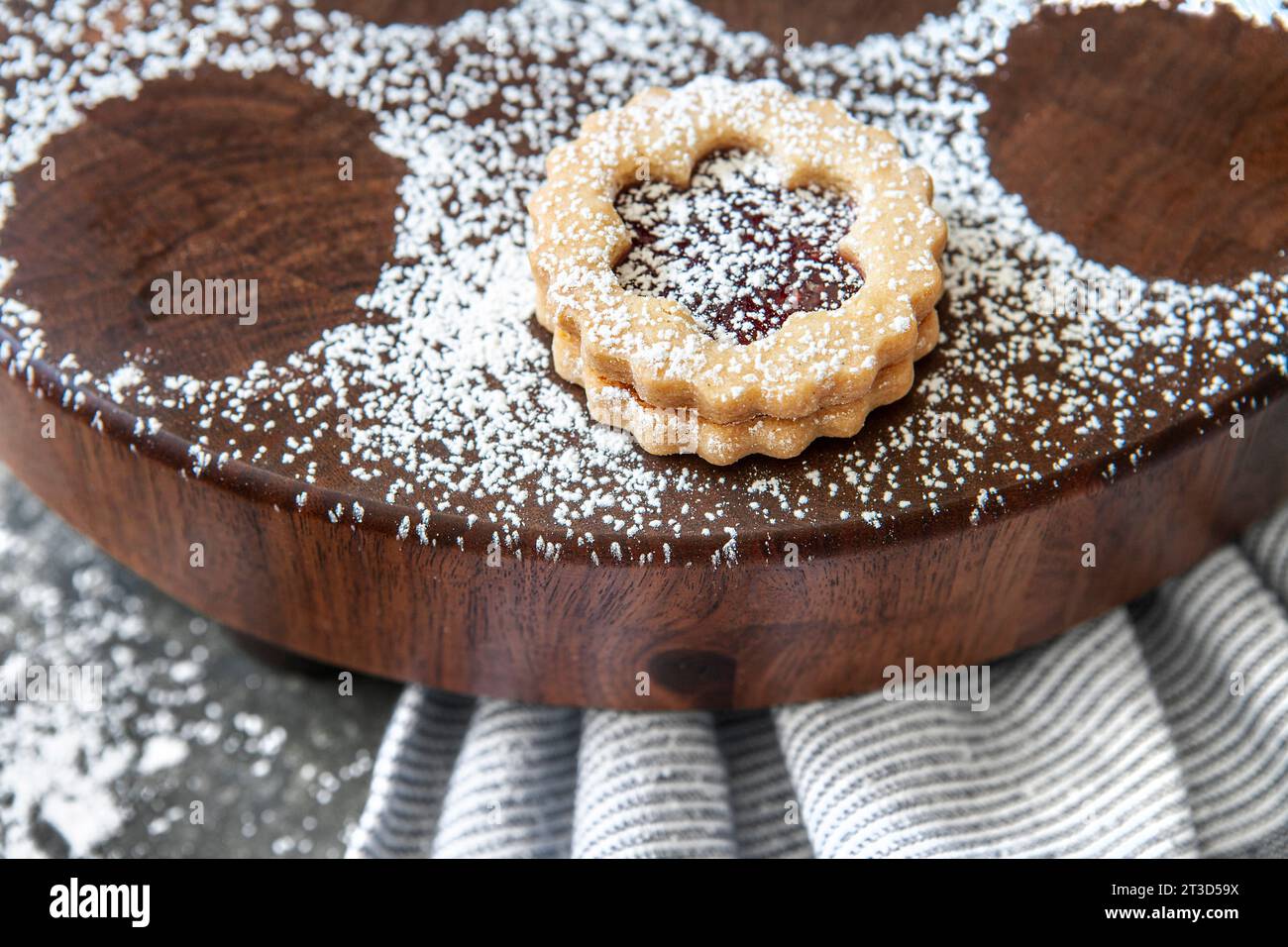 Close-up of one Linzer cookie dusted with powdered sugar on round wood board Stock Photo