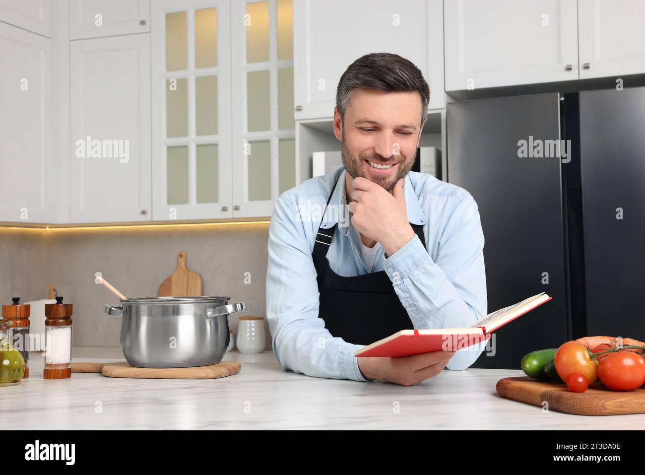 Adult man reading recipe book at white marble table in kitchen Stock Photo