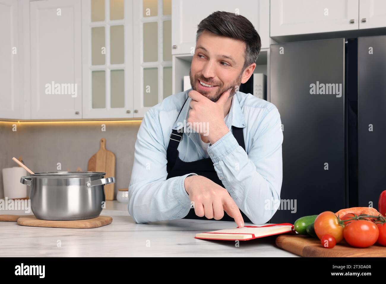Adult man reading recipe book at white marble table in kitchen Stock Photo