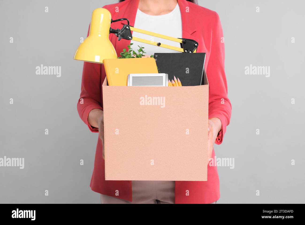 Unemployed woman with box of personal office belongings on grey background, closeup Stock Photo