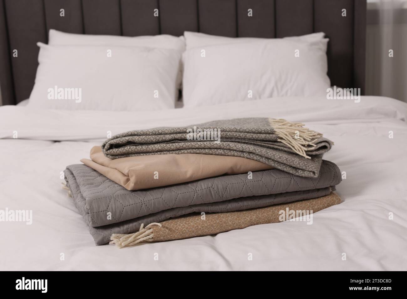 Stack of different folded blankets on bed in room. Home textile Stock Photo