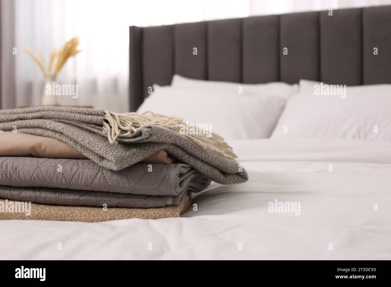 Stack of different folded blankets on bed in room, space for text. Home textile Stock Photo