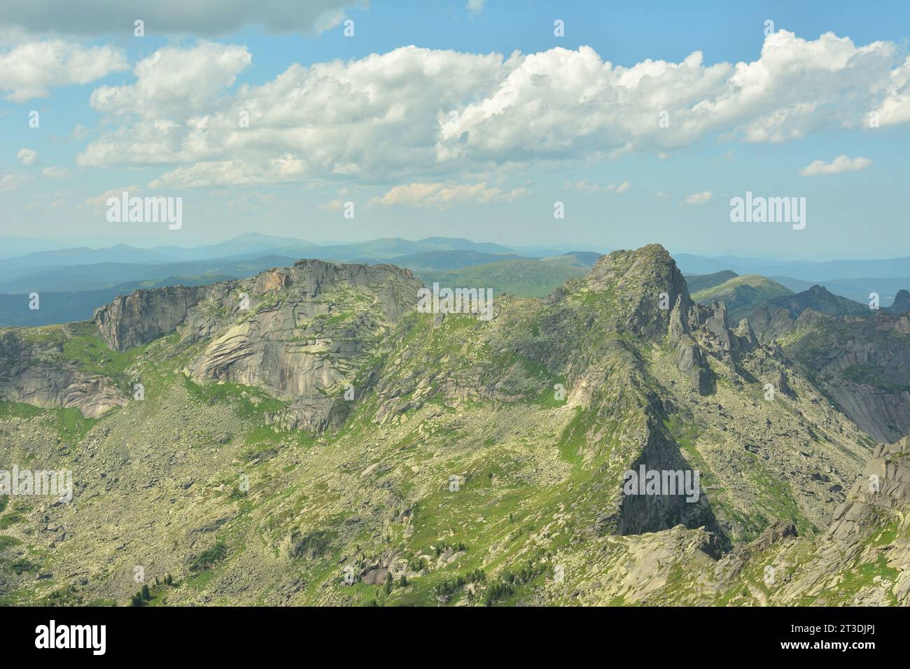 A high rocky massif with peaked peaks partially overgrown with grass under a cloudy summer sky. Natural park Ergaki, Krasnoyarsk region, Siberia, Russ Stock Photo