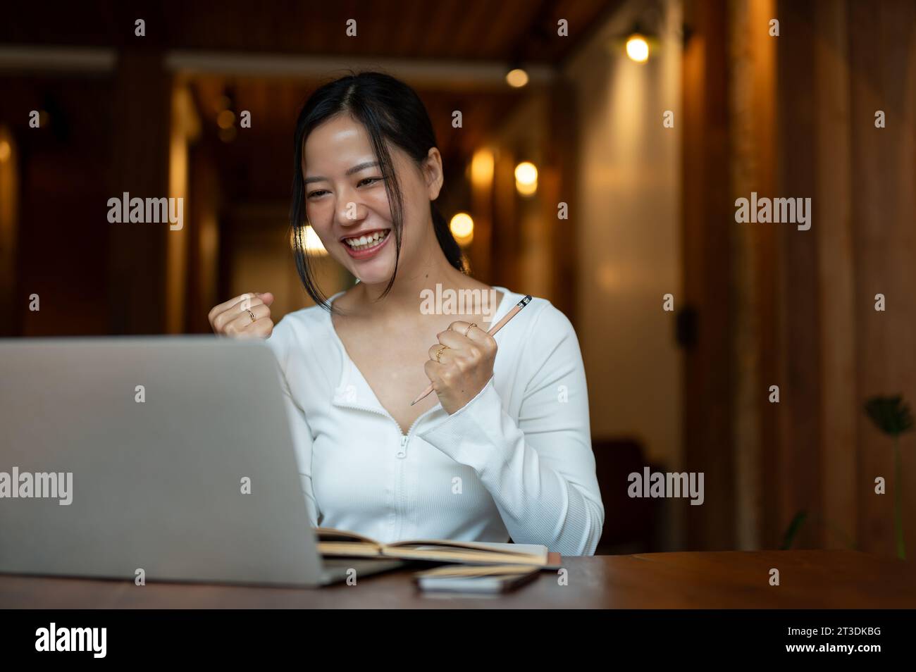 A cheerful and beautiful Asian woman is looking at her laptop screen ...