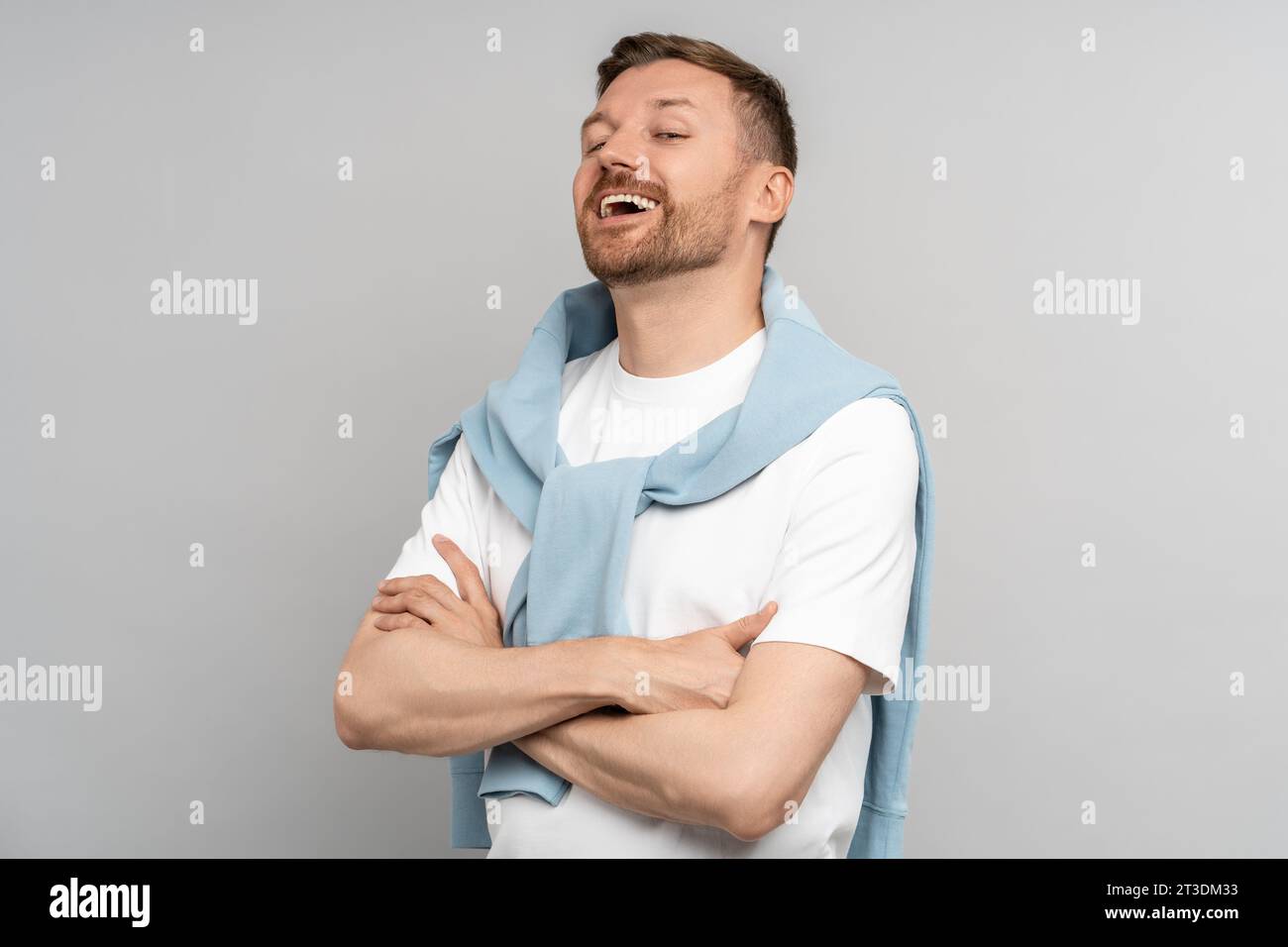 Laughing satisfied arrogant humorist with hands folded on chest standing on gray background.  Stock Photo