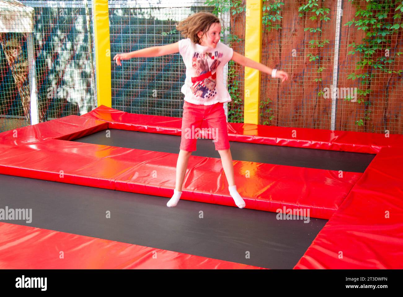 Happy girl having fun while jumping on trampoline. Sports girl jumps on a trampoline. Outdoor shot of girl jumping on trampoline, enjoys jumping in ho Stock Photo