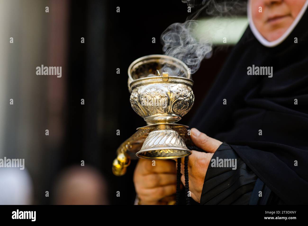 Shallow depth of field (selective focus) details with the hand of a orthodox Christian nun holding a smoking metallic censer incense burner Stock Photo