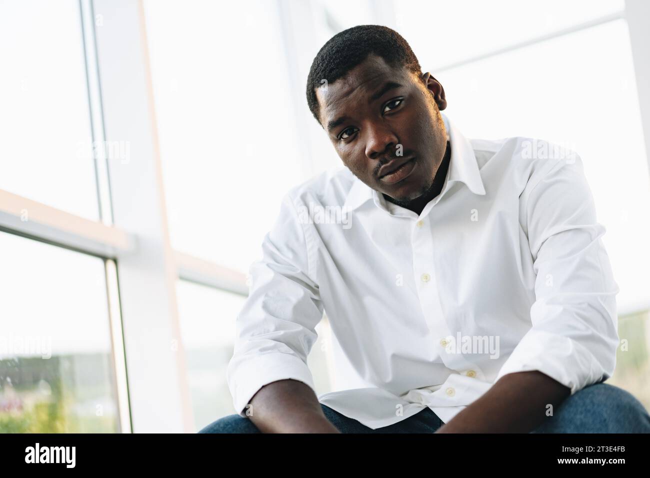 Young african man in white shirt and glasses posing near large window ...